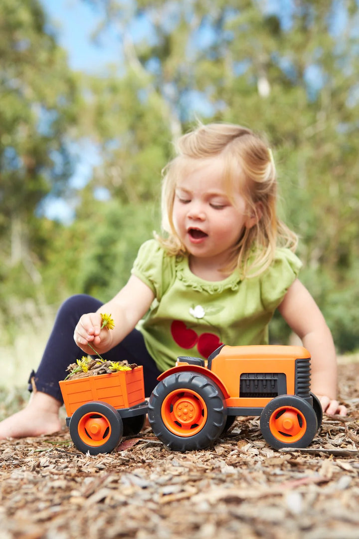 Child playing with a toy tractor and trailer outdoors
